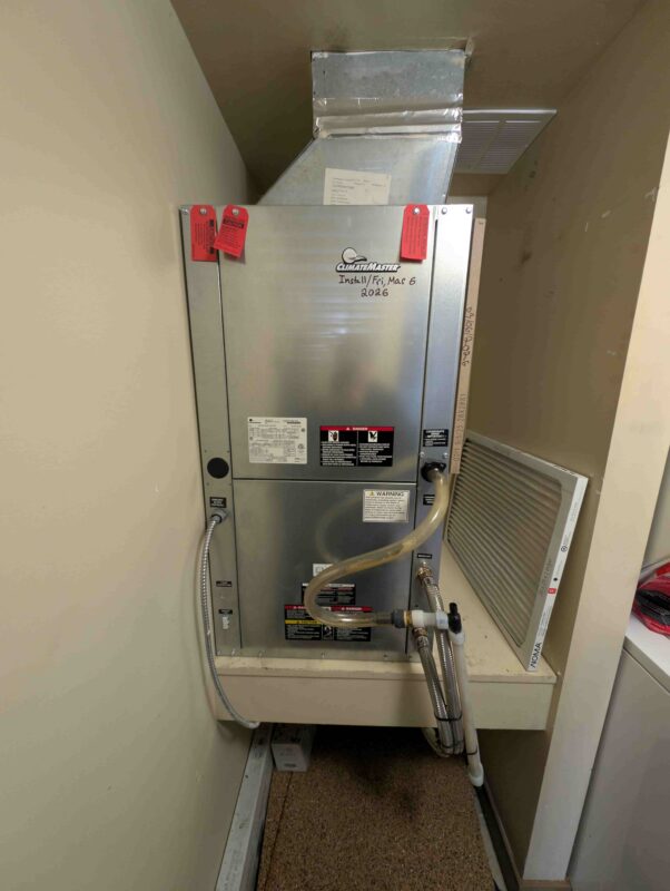 A newly installed ClimateMaster heat pump unit inside a residential utility closet, showing clean ductwork and piping connections.