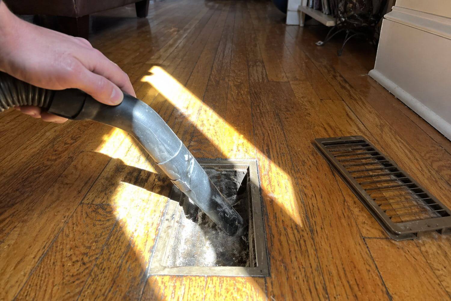 Vacuuming dust and debris from a home floor vent to improve airflow as part of a Calgary spring HVAC checklist.